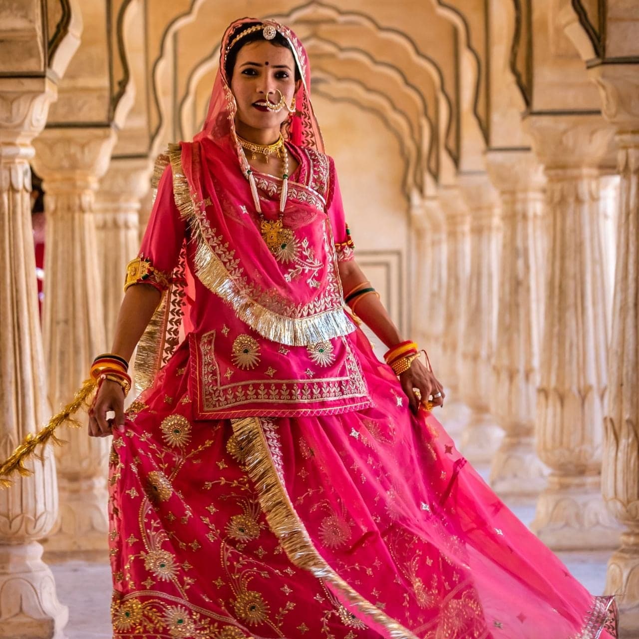 A woman in a pink and gold Rajasthani lehenga dancing in a pillared marble hall