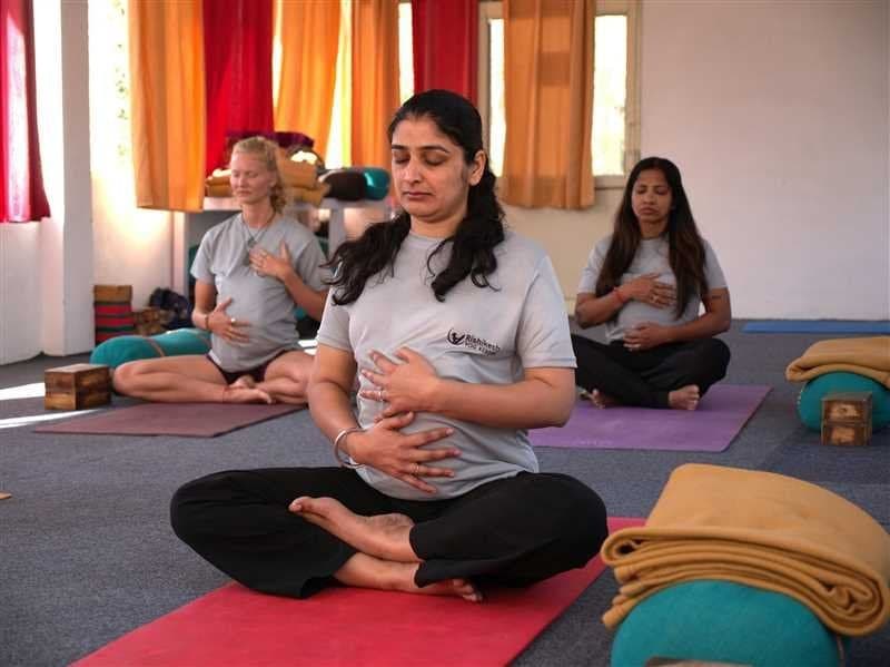 Three women seated cross-legged in a yoga studio, practising breathing with hands on chest and belly