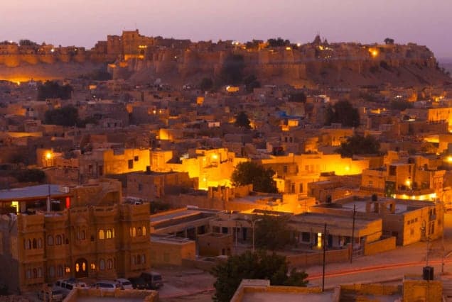 The old city of Jaisalmer lit up at dusk, with the fort on the hill above