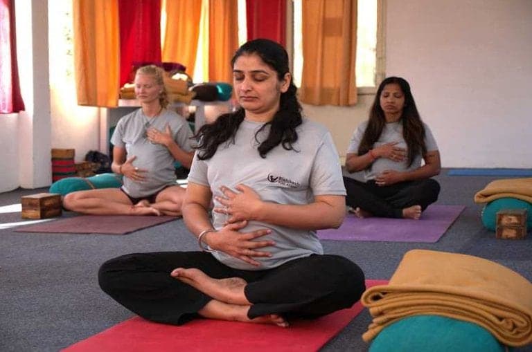 Yoga teacher training students seated cross-legged, practising breathing in a studio