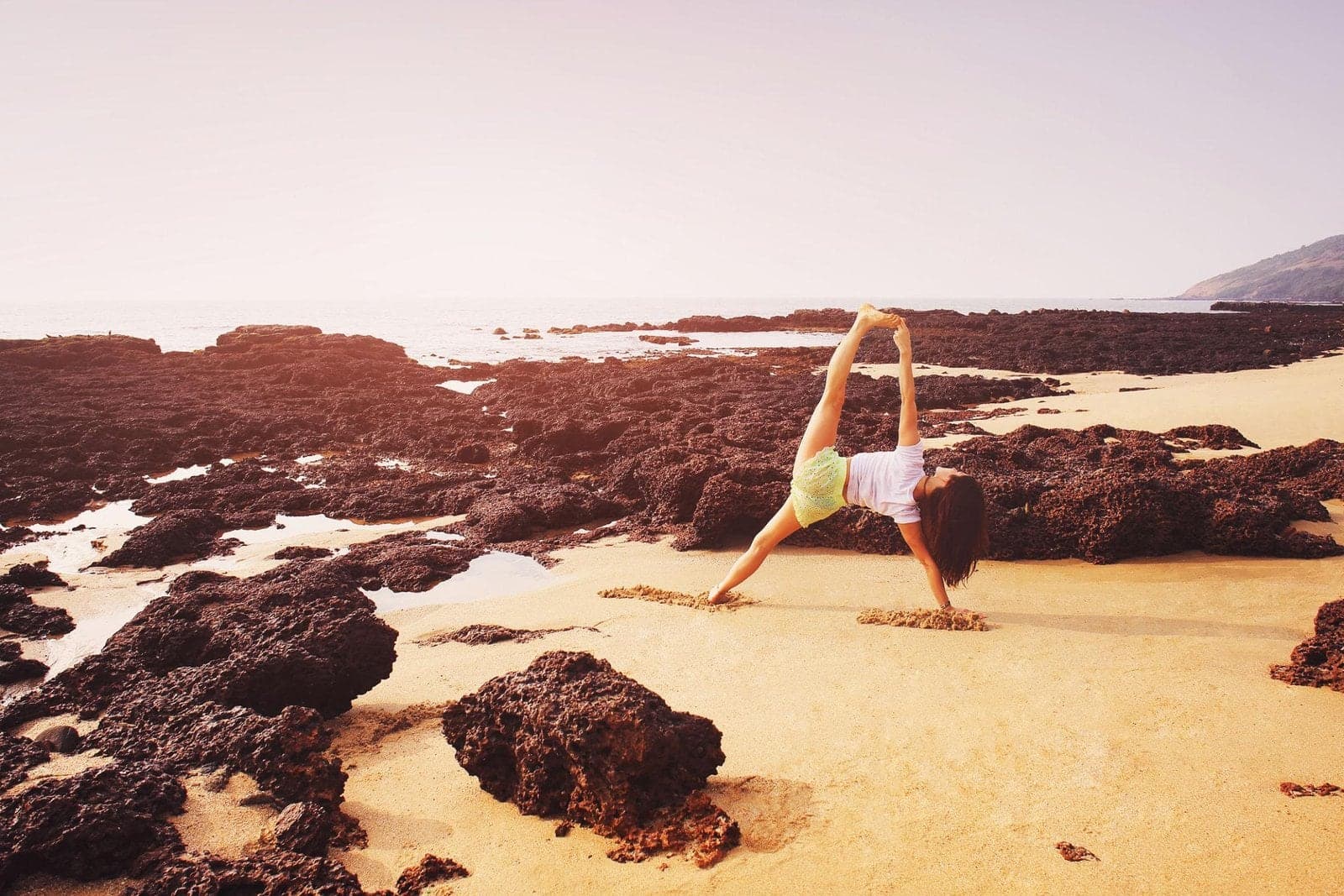 A woman holding a side plank yoga pose on a rocky beach