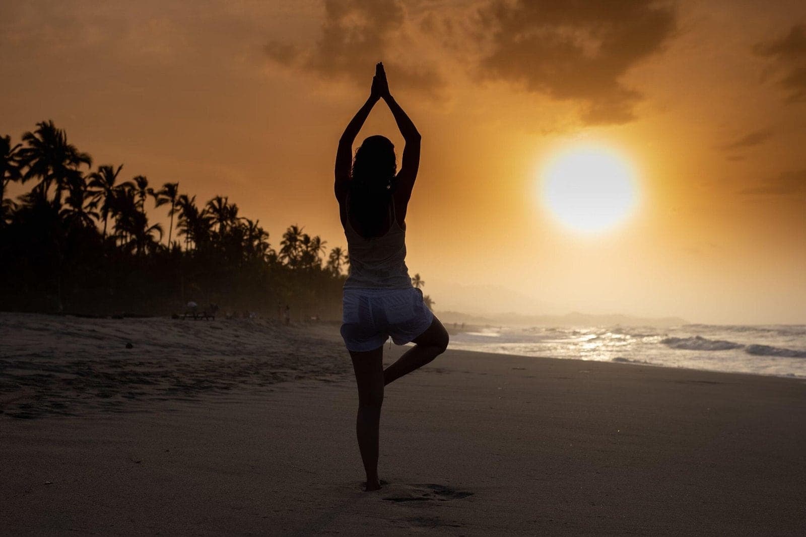 Silhouette of a woman in tree pose on a beach at sunset