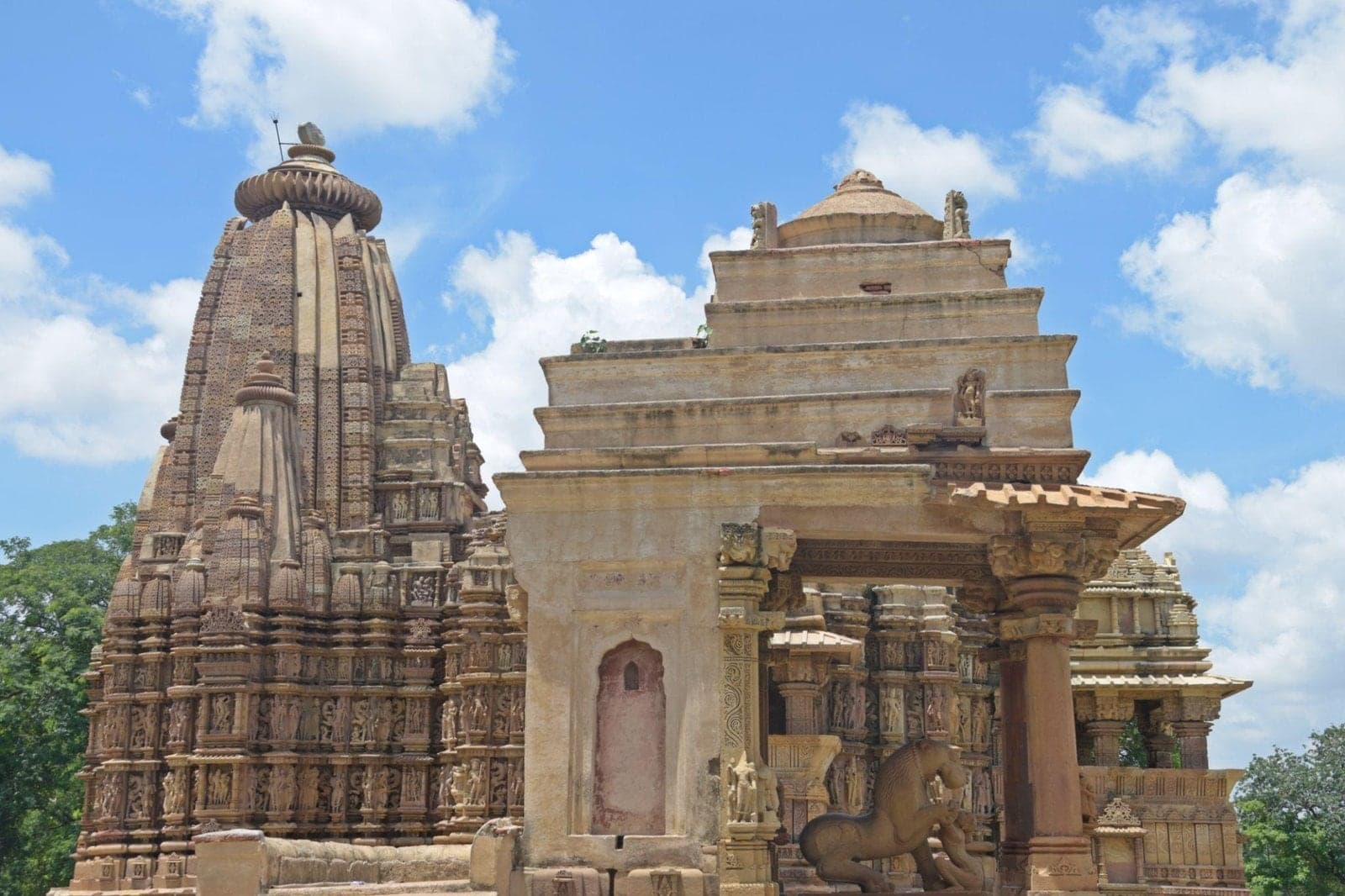 Sandstone temples at Khajuraho with a carved lion statue, under a blue sky
