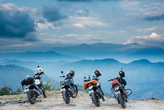 Four loaded touring motorcycles parked on a ridge above layers of blue mountains