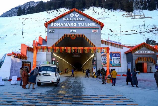 Travellers and a car at the entrance of the Sonamarg tunnel in snow, decorated with marigold garlands
