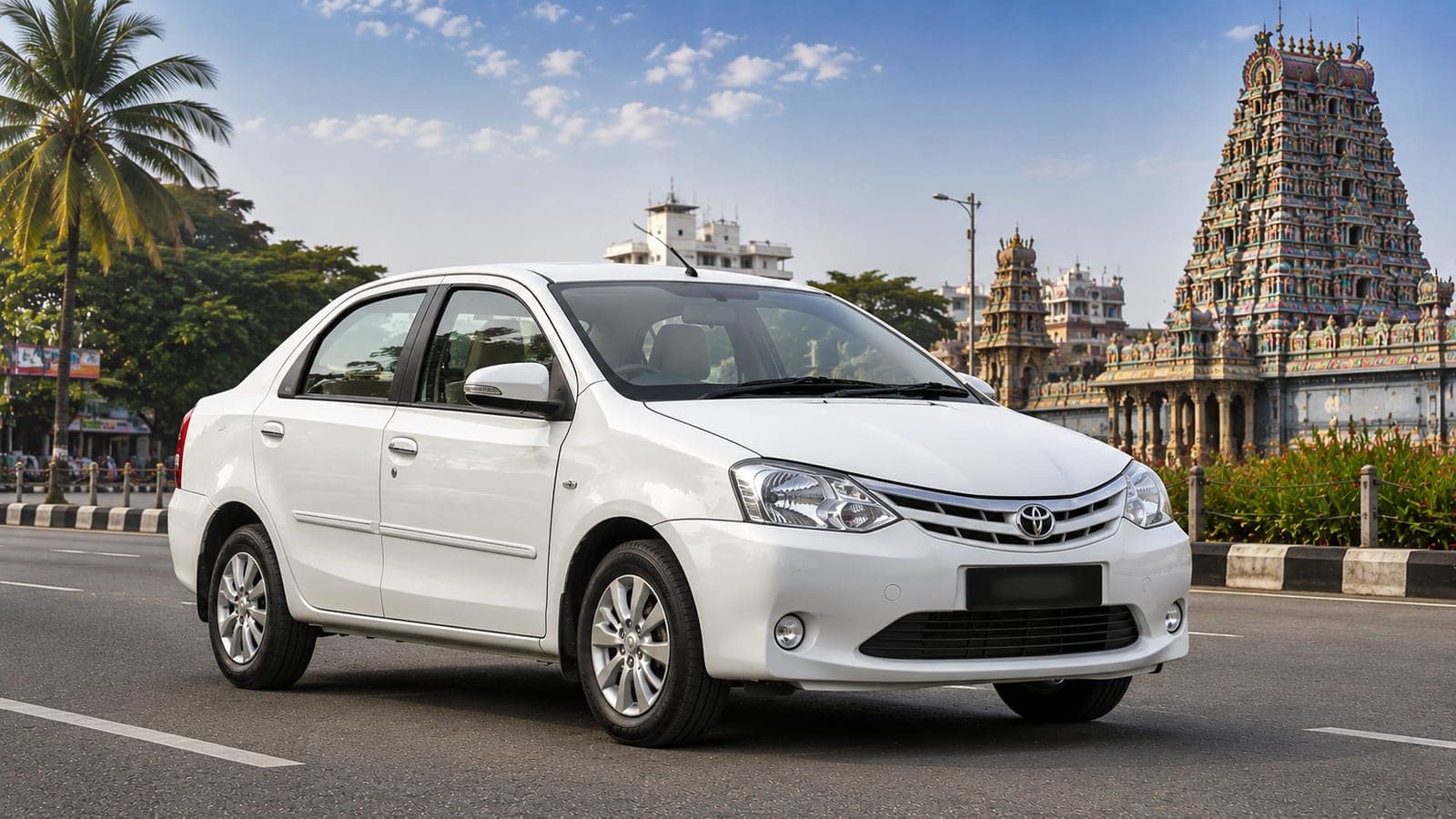 White Toyota Etios sedan on a road near a South Indian temple tower