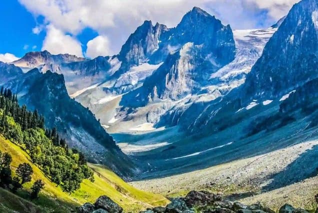 Snow-streaked peaks above a green Kashmir valley and pine-covered slopes