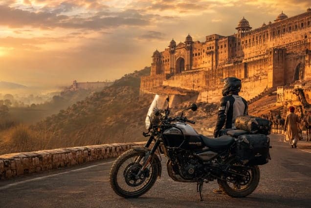 A motorcyclist beside a loaded adventure bike on the road below Amber Fort at sunrise