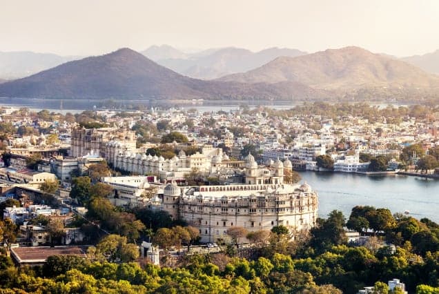 The City Palace and old city of Udaipur on the shore of Lake Pichola, with hills behind