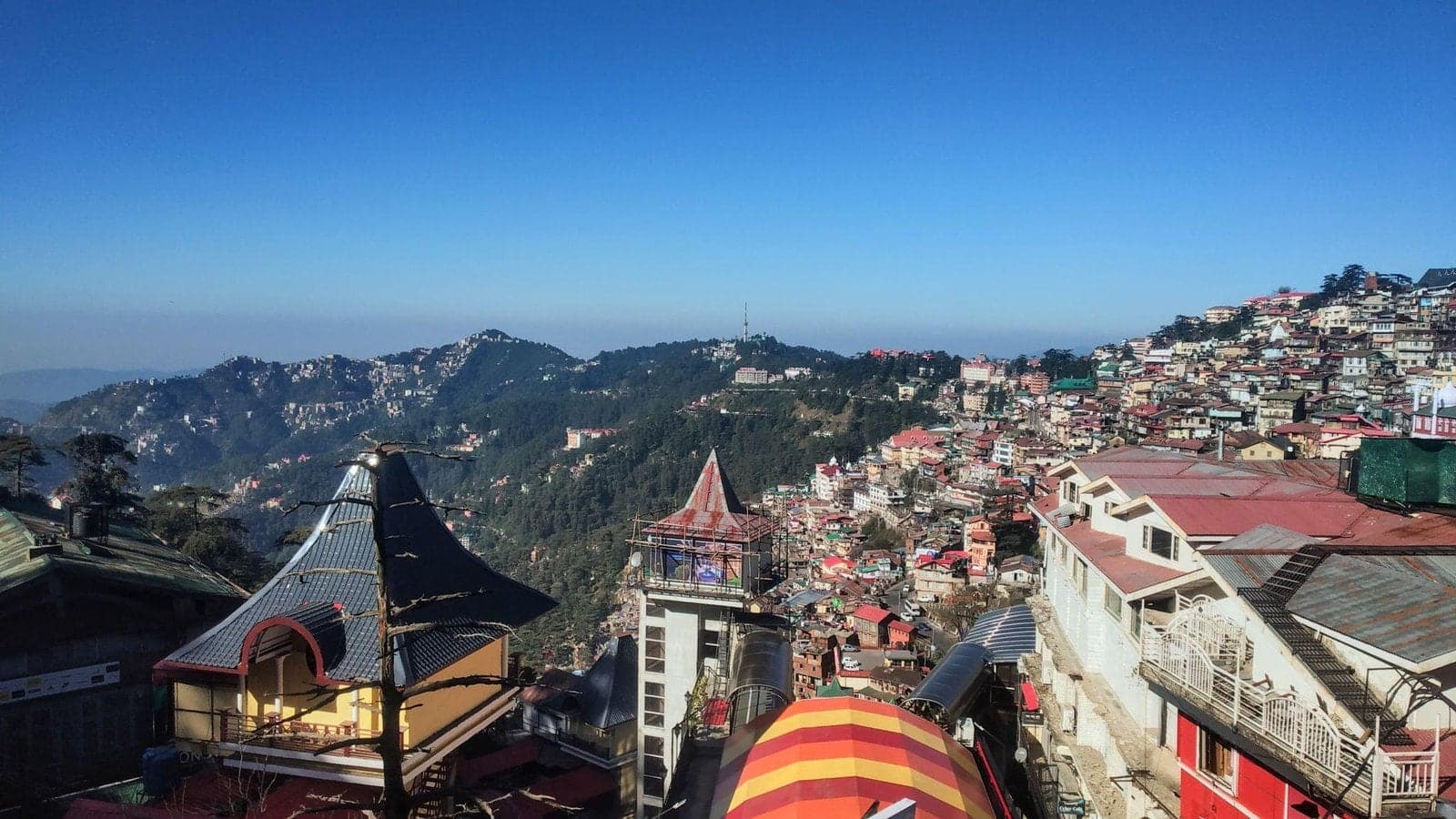 A Himalayan hill town spread across forested ridges under a clear blue sky