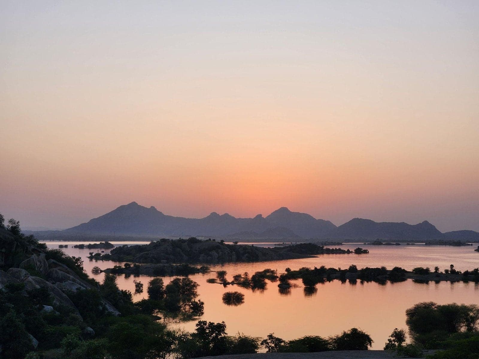 Sunset over a lake scattered with rocky islands, with granite hills on the horizon