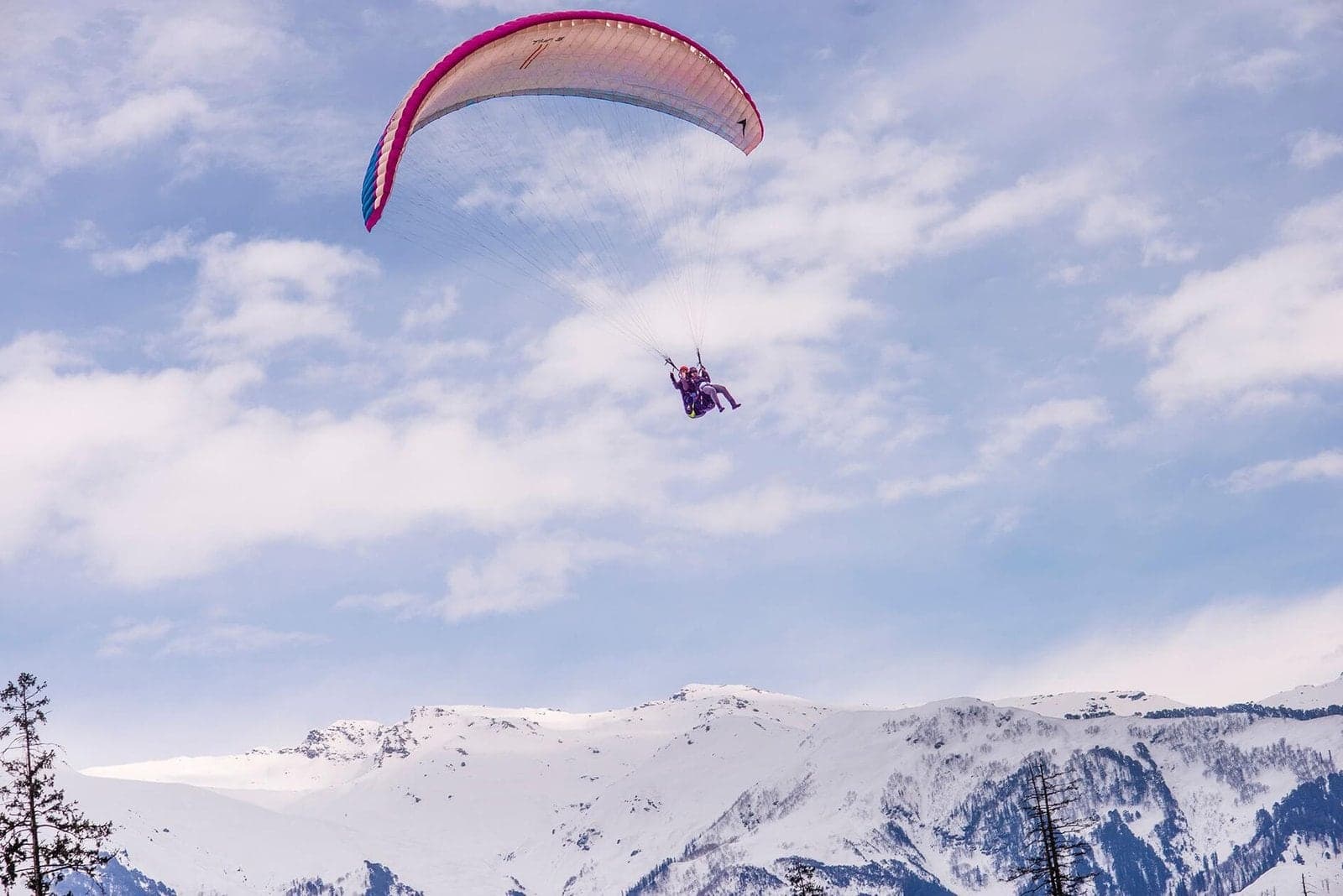 A paraglider flying high above snow-covered mountains