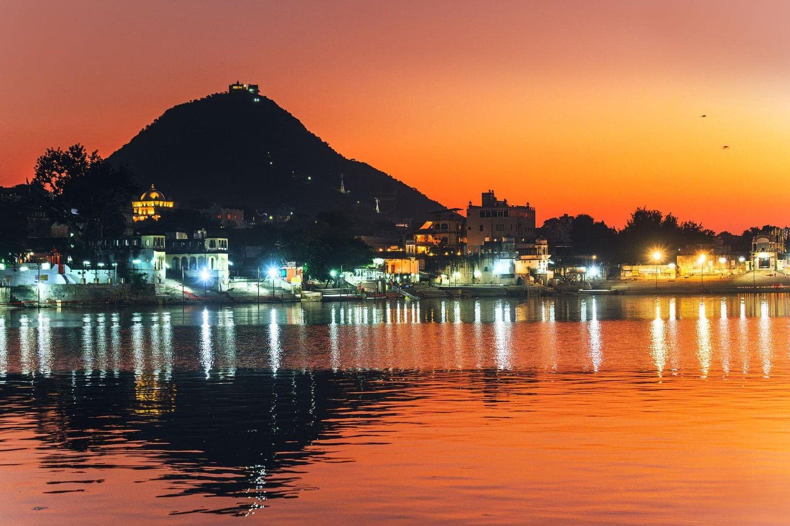Pushkar Lake at dusk, with the lights of the town and the Savitri Temple hill reflected in the water