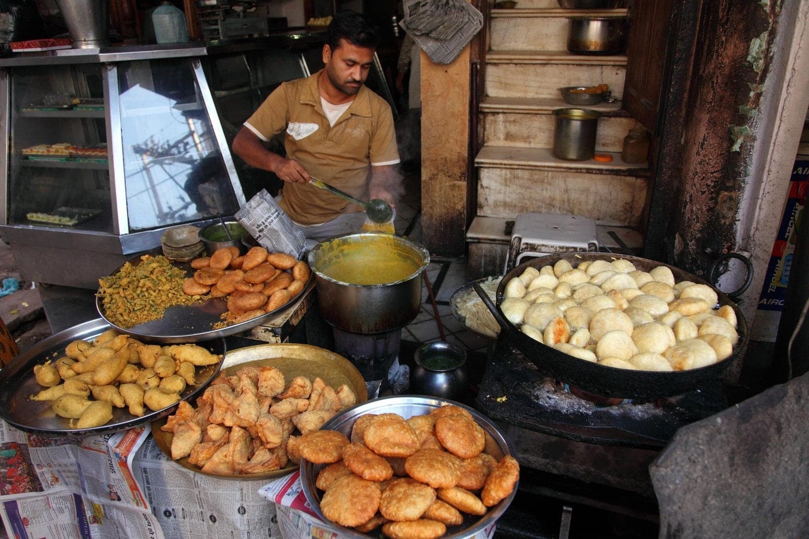 A cook frying kachoris and samosas in large pans at a street food shop